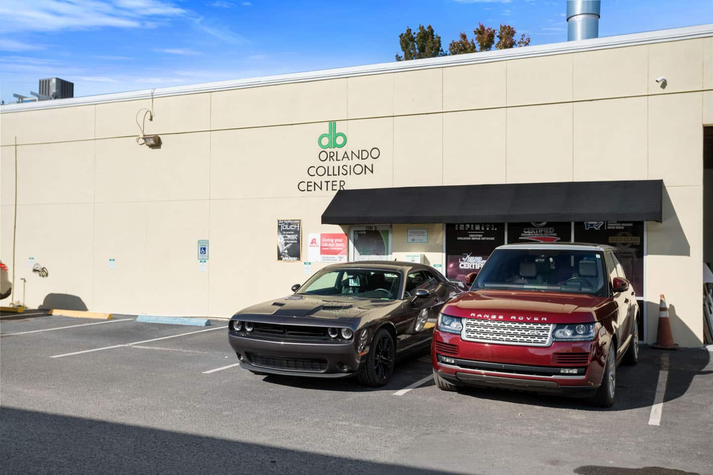 DB Orlando Collision Center exterior with a gray Dodge Challenger and a red Range Rover parked in front, highlighting auto body repair services and factory-certified collision repairs.