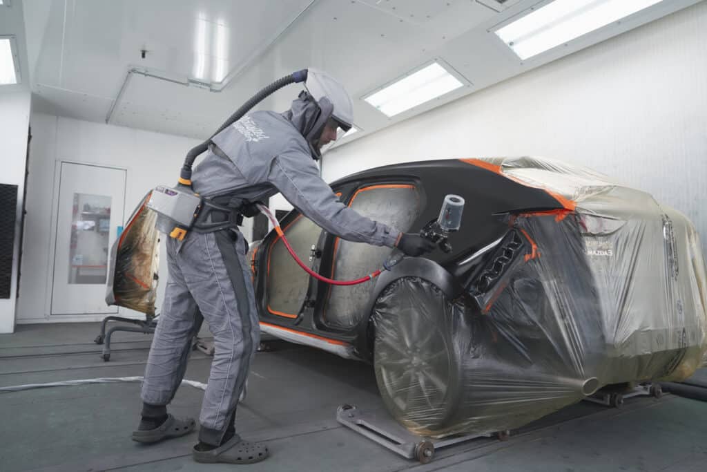Auto body technician applying paint to a vehicle in a spray booth, showcasing precision in collision repair and restoration services at an auto body shop.