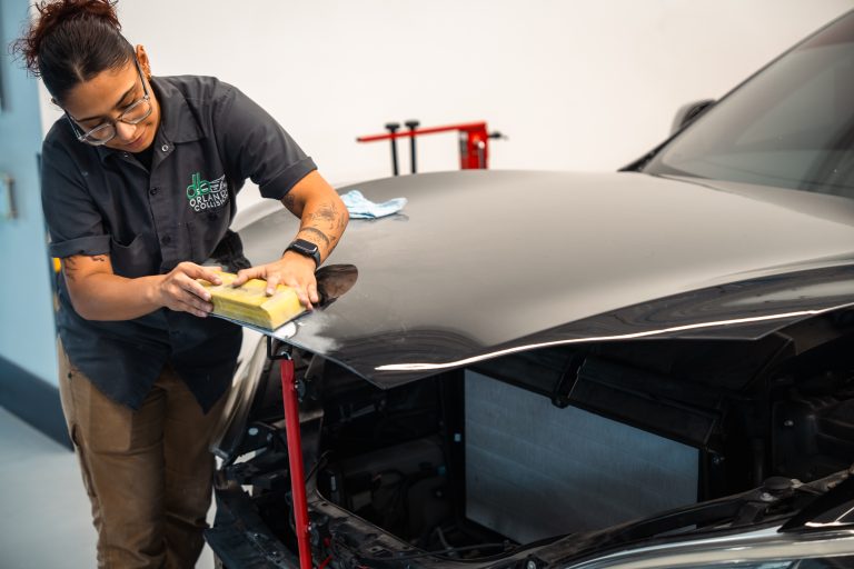Auto body technician performing detailed repair work on a vehicle's hood at DB Orlando Collision, emphasizing professional autobody repairs and high-quality service in an auto body shop.