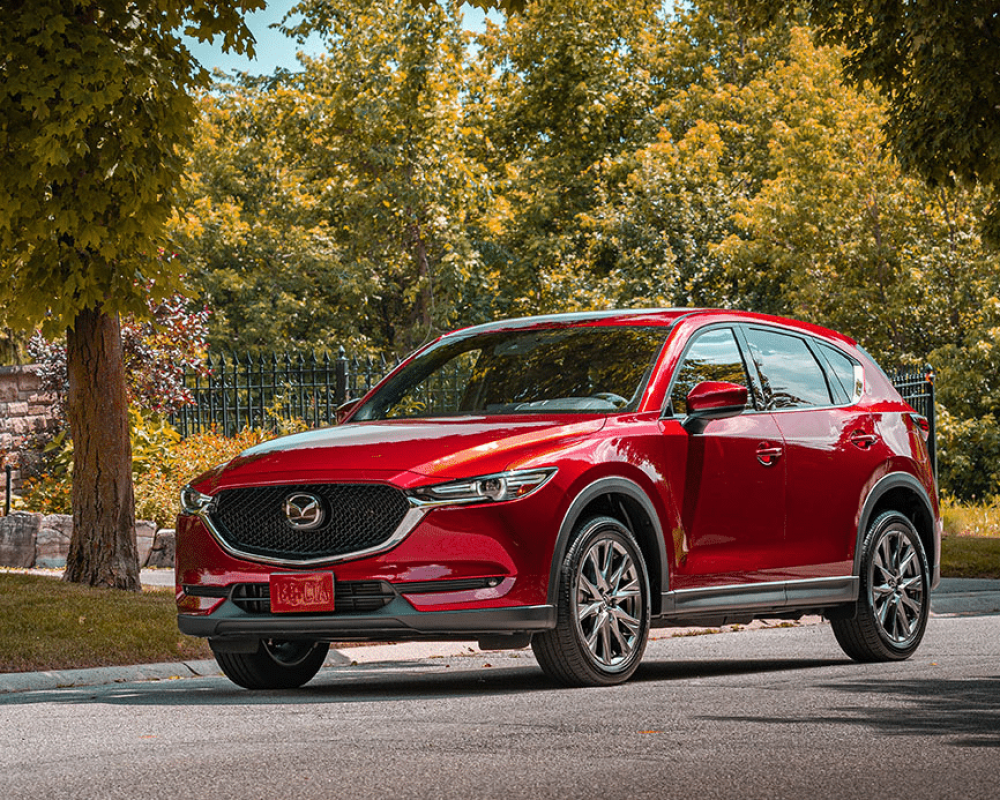 Red Mazda CX-5 parked on a tree-lined street, showcasing its sleek design and premium features, representing certified Mazda collision repair services by db Orlando Collision.